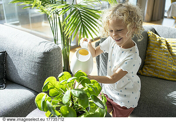 Smiling girl with blond hair watering plant at home