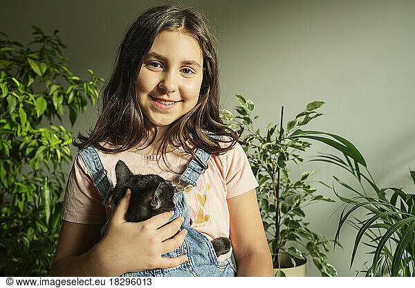 Smiling girl with cat in front of plants at home