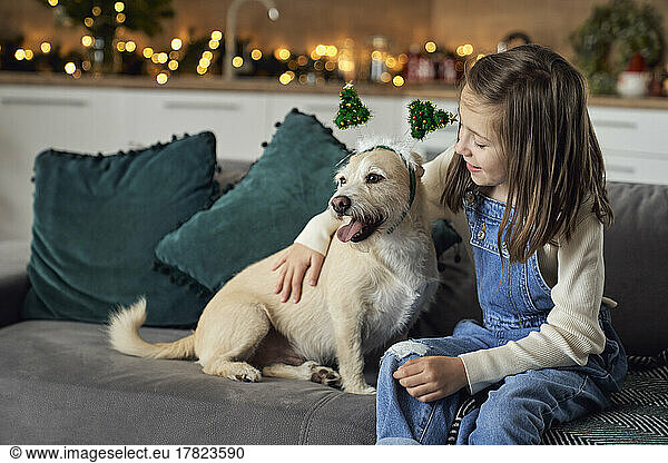 Smiling girl with dog sitting on sofa at home