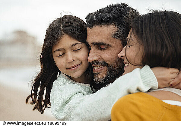 Smiling girl with eyes closed hugging mother and father