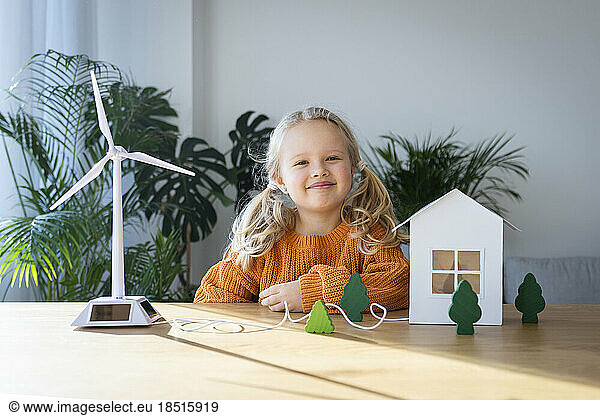 Smiling girl with house and wind turbine models on desk
