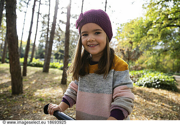 Smiling girl with knit hat holding bicycle handle at park