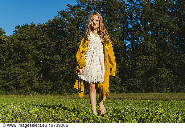 Smiling girl with long hair walking on grass in front of trees