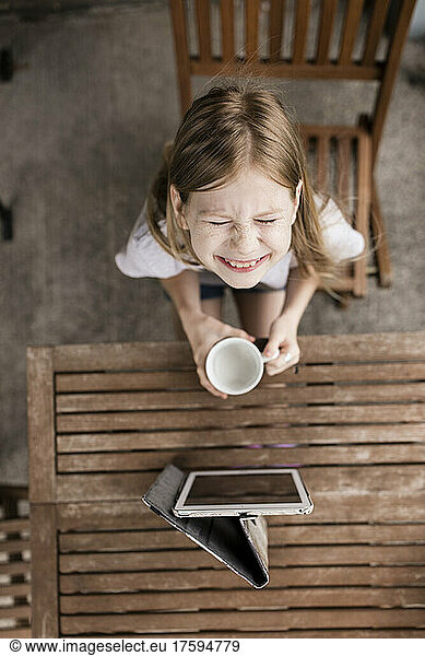 Smiling girl with milk cup and tablet PC on table
