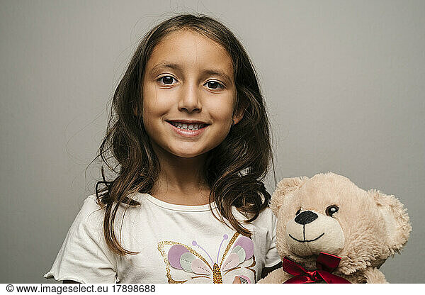 Smiling girl with teddy bear against gray background