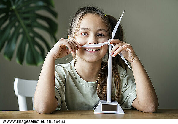 Smiling girl with wind turbine model at home