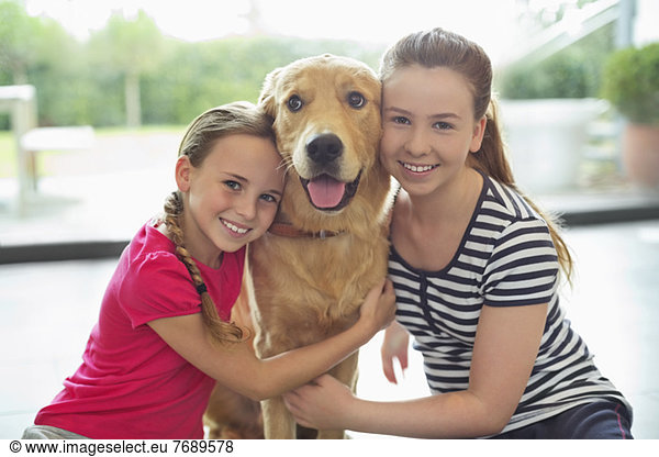 Smiling girls hugging dog indoors