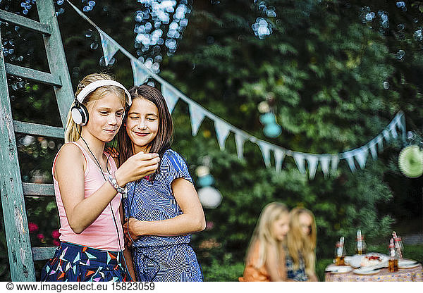 Smiling girls with headphones and cell phone on a birthday party outdoors