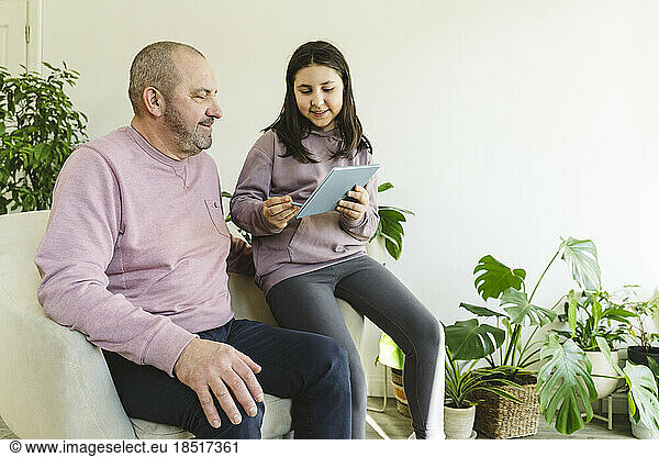 Smiling granddaughter sharing tablet PC with grandfather at home