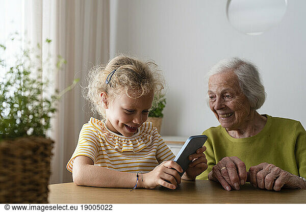 Smiling granddaughter using smart phone by grandmother at home