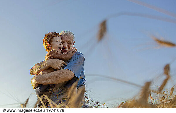 Smiling grandfather hugging grandson under sky