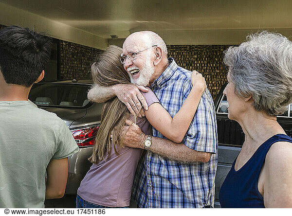 Smiling grandfather hugs teen granddaughter as grandmother looks on.