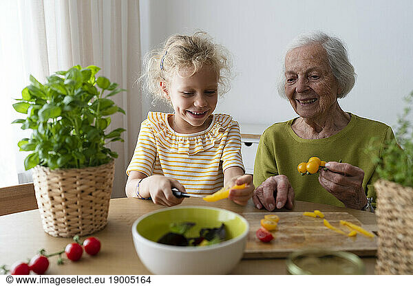 Smiling grandmother and granddaughter examining vegetables on table