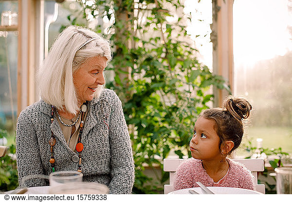 Smiling grandmother looking at granddaughter while having lunch