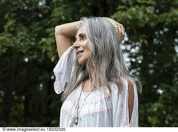 Smiling gray haired woman with arm raised at forest