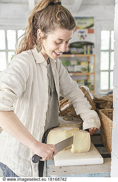 Smiling grocer cutting cheese in greengrocer shop