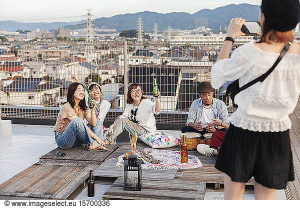 Smiling group of young Japanese men and women on a rooftop in an urban setting.