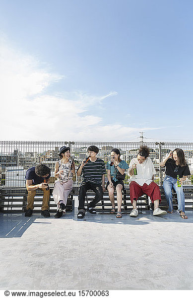 Smiling group of young Japanese men and women sitting on a rooftop in an urban setting.