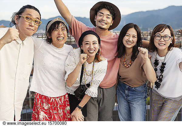 Smiling group of young Japanese men and women standing on a rooftop in an urban setting.