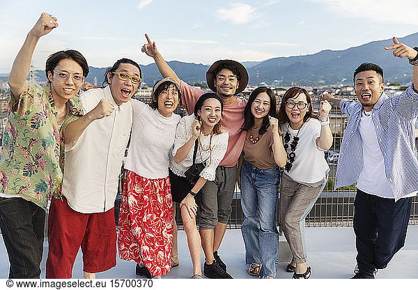 Smiling group of young Japanese men and women standing on a rooftop in an urban setting.