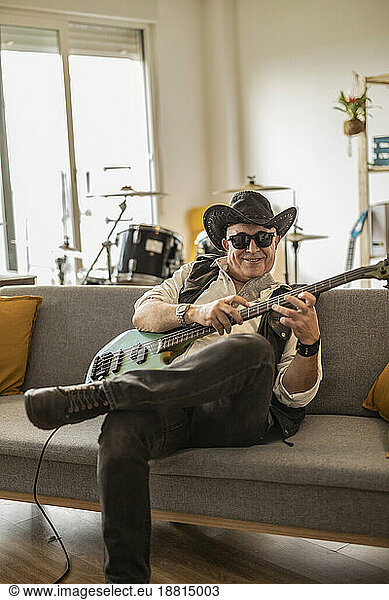 Smiling guitarist wearing hat and practicing guitar at home