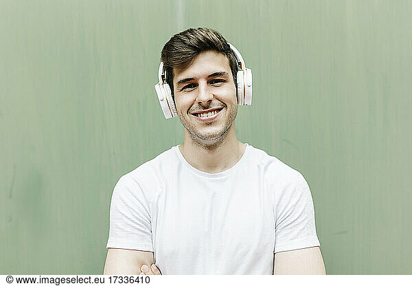 Smiling handsome man wearing headphones in front of wall