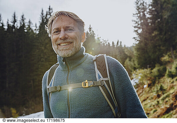 Smiling handsome man with backpack standing in forest against sky at Salzburger Land  Austria