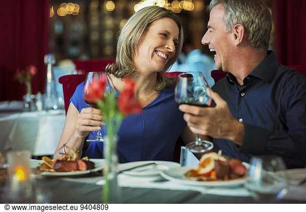 Smiling happy mature couple looking at each other and holding glasses with red wine in restaurant