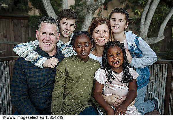 Smiling happy multiracial family hugging in front of tree
