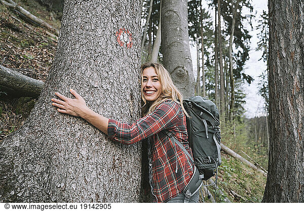 Smiling hiker embracing tree in forest