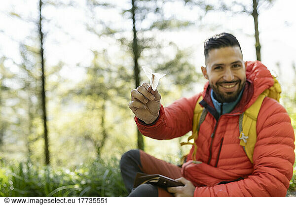 Smiling hiker with paper airplane sitting in forest