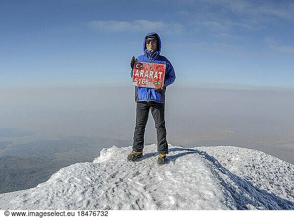 Smiling hiker with signboard on Mt Ararat peak at sunny day