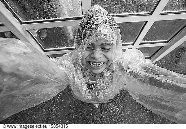 Smiling kid wearing a raincoat in the rain close to a glass door