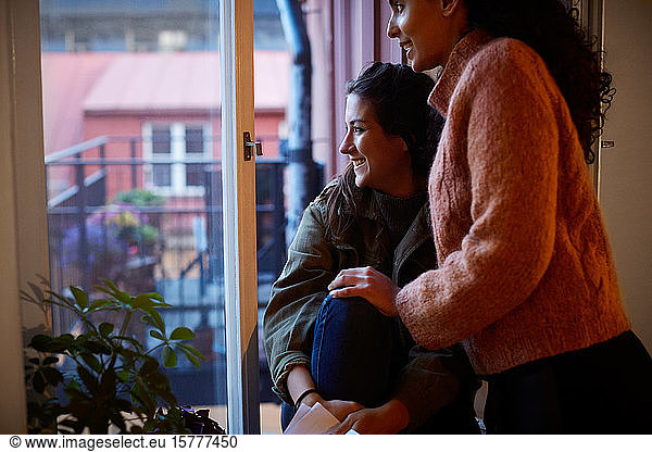 Smiling lesbian couple looking through window at apartment during vacation