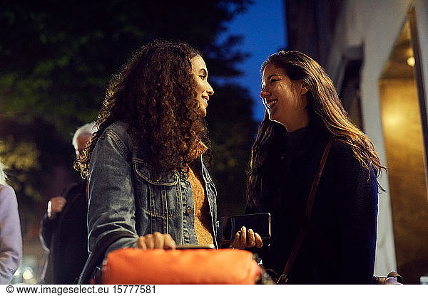 Smiling lesbian couple standing on sidewalk in city at night