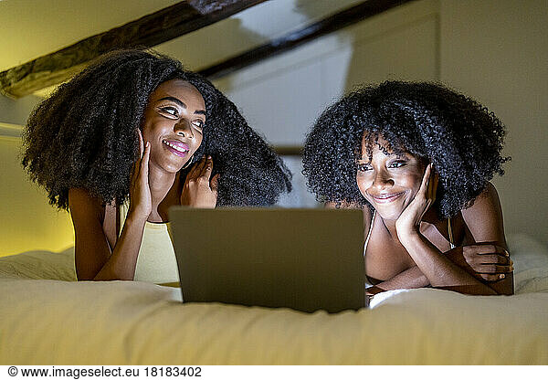 Smiling lesbian couple watching movie in bedroom at home