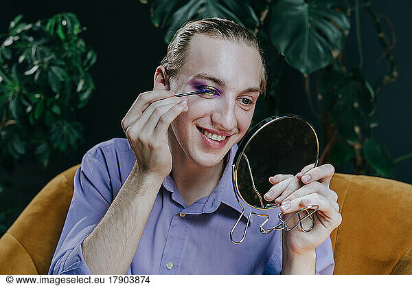 Smiling make-up artist applying mascara looking in mirror