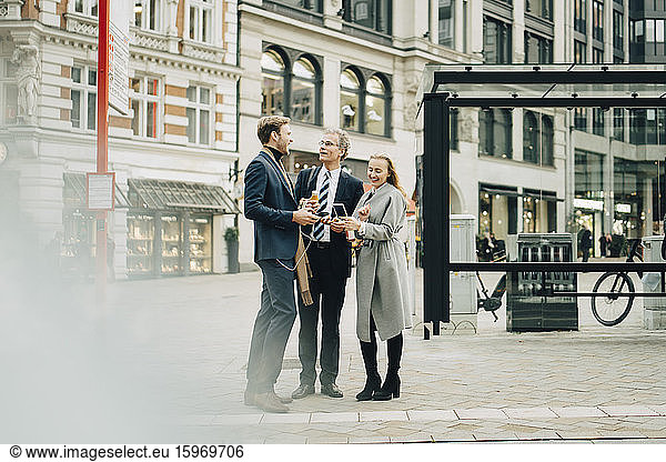 Smiling male and female business colleagues talking while standing in city