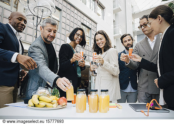 Smiling male and female business executives with juice outside office
