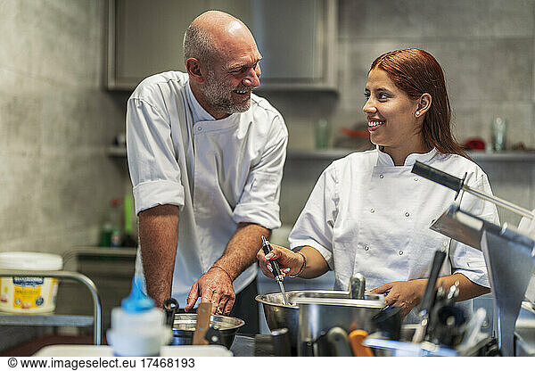 Smiling male and female chefs talking while cooking in kitchen
