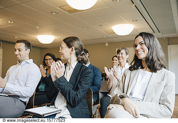 Smiling male and female clapping while sitting in office workshop