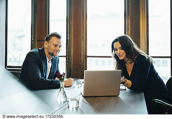 Smiling male and female colleagues discussing over laptop in board room at office