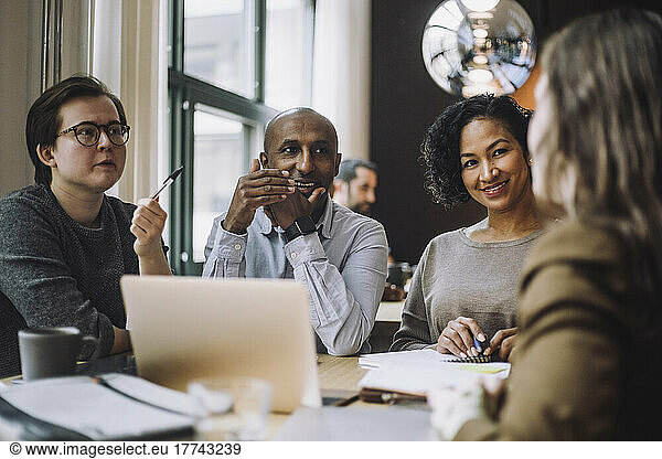 Smiling male and female colleagues looking at businesswoman discussing plan at desk in creative office
