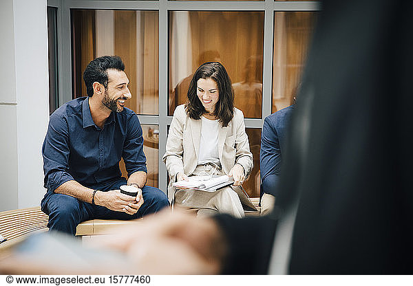 Smiling male and female entrepreneurs talking while sitting against office