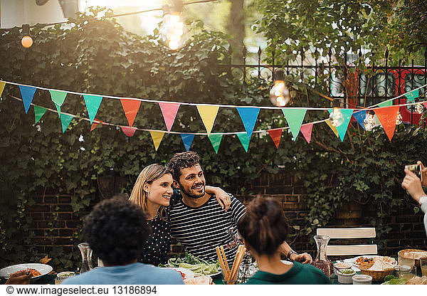 Smiling male and female friends posing for photograph during dinner party in backyard