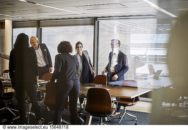 Smiling male and female lawyers shaking hands while greeting each other at board room in office