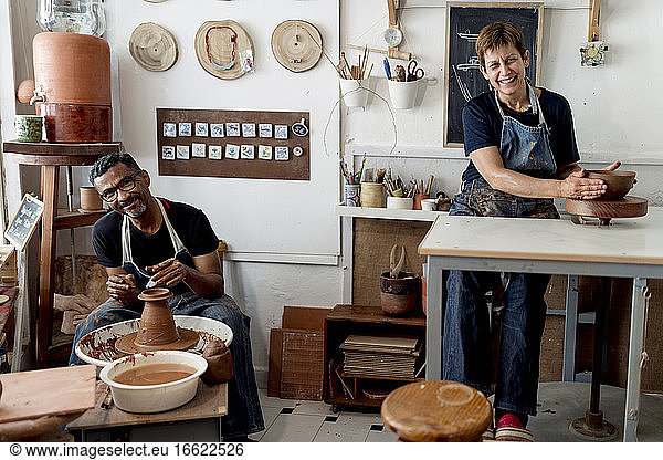 Smiling male and female potters working in workshop