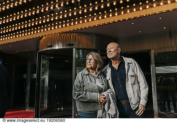 Smiling male and female senior friends standing outside movie theater