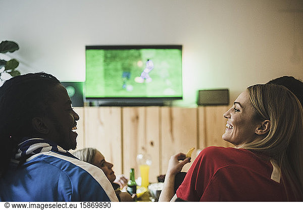 Smiling male and female watching soccer while sitting with friends at home
