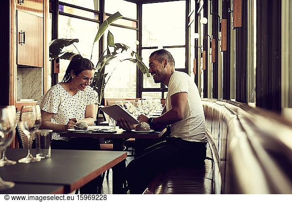 Smiling male and female with digital tablet sitting at table in cafe
